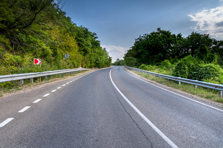 Road landscape forest and mountain. Empty long mountain road to the horizon on a sunny summer day with dramatic cloudy sky. Highway turn panoramic view.の写真素材