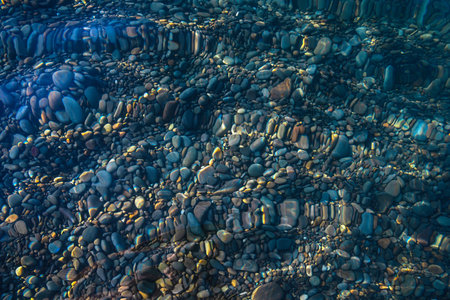 Underwater pebble backgrounds. Colorful stones sea bottom and sea fish in the sun rays. View from above through clear water. Seascape wallpaper texture.の写真素材