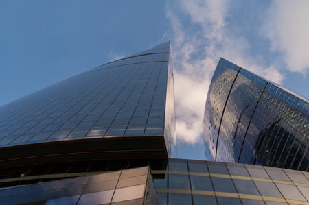 Angled view of modern skyscrapers in business district against blue sky. Looking Up high-rise office buildings. Evening time, sunset. Orange, yellow and gold shades of color.の写真素材