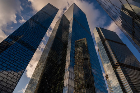 Skyscrapers in business district against blue sky. Looking up high-rise office buildings. Evening time, sunset. Orange, yellow and gold shades of color. Angled view.の写真素材