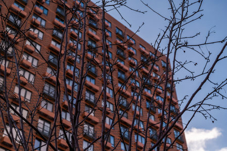 Apartment skyscraper through the branches of autumn trees in business district against blue sky. Looking up high-rise residential buildings. Day time, park, fall. Angled view. Defocus background.の写真素材