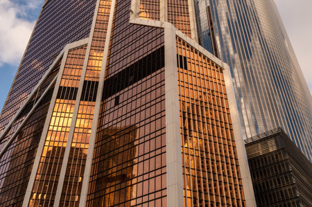 Skyscrapers in business district against blue sky. Looking up high-rise office buildings. Evening time, sunset. Orange, yellow and gold shades of color. Angled view.の写真素材
