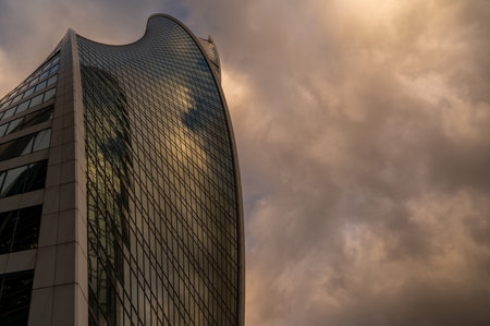 Skyscrapers in business district against blue sky. Looking up high-rise office buildings. Evening time, sunset. Orange, yellow and gold shades of color. Angled view.の写真素材