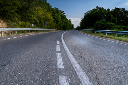 Road turn. Landscape highway, forest, mountains and sky on the horizon. Empty long mountain road to the horizon on a sunny summer day with dramatic cloudy sky. Highway turn panoramic view.の写真素材