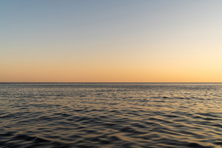 Blue sea surface with to the horizon. Sea waves with cloudy sky. Orange bright sunlight in seawater. Abstract background of water flow in ocean, sea, river, lake.の写真素材