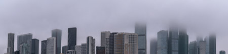 City building pano. Skyscrapers in business district against gray foggy sky. Panoramic view of high-rise office buildings. Panorama cityscape. Long wide banner.の写真素材