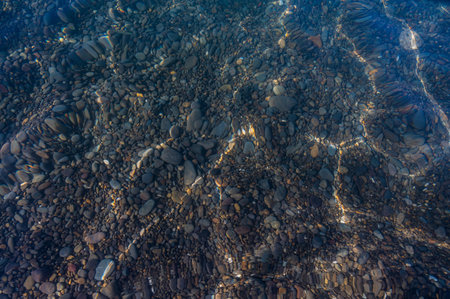Underwater pebble backgrounds. Colorful stones sea bottom in the sun rays. View from above through...