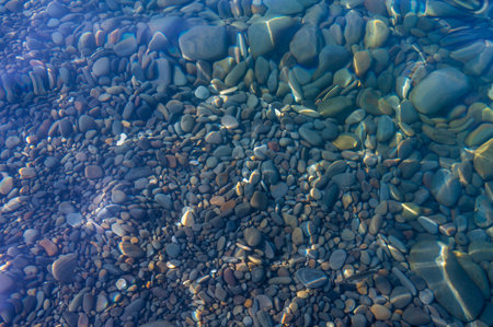 Underwater pebble backgrounds. Colorful stones sea bottom in the sun rays. View from above through clear water. Seascape wallpaper texture. Soft focus.の写真素材
