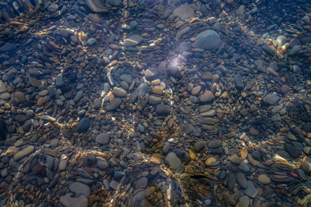Underwater pebble backgrounds. Colorful stones sea bottom in the sun rays. View from above through clear water. Seascape wallpaper texture. Soft focus.の写真素材