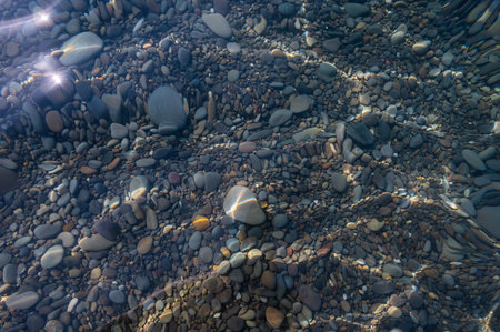 Underwater pebble backgrounds. Colorful stones sea bottom in the sun rays. View from above through clear water. Seascape wallpaper texture. Soft focus.の写真素材