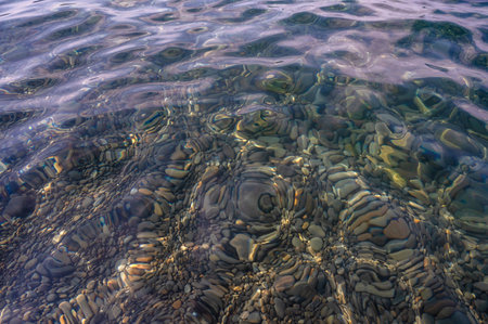 Underwater pebble backgrounds. Colorful stones sea bottom in the sun rays. View from above through clear water. Seascape wallpaper texture. Soft focus.の写真素材