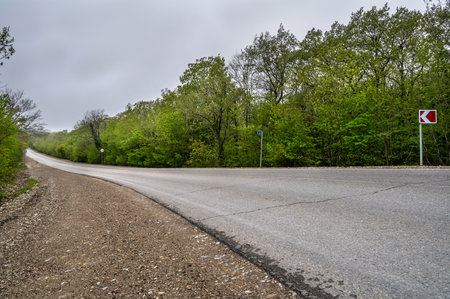 Road landscape in forest. Empty long mountain road to the horizon with dramatic cloudy sky. Highway turn panoramic view.の写真素材