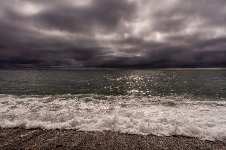 Sun between dark storm clouds over ocean. Dramatic seascape. Clouds and rain flurry over sea.の写真素材