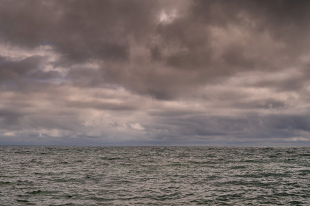 Sun between dark storm clouds over ocean. Dramatic seascape. Clouds and rain flurry over sea.の写真素材