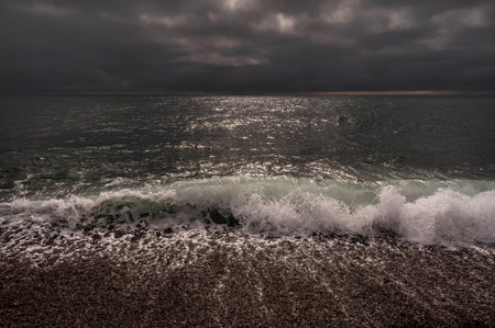 Sun between dark storm clouds over ocean. Dramatic seascape. Clouds and rain flurry over sea.の写真素材