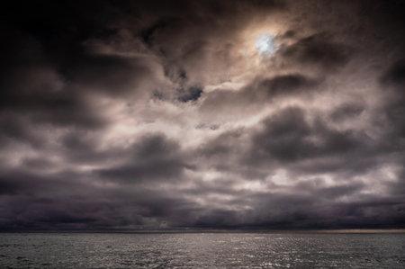 Sun between dark storm clouds over ocean. Dramatic seascape. Clouds and rain flurry over sea.の写真素材