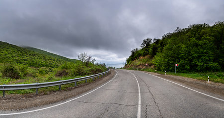 Empty long mountain road to the horizon on a sunny summer day with dramatic cloudy sky. Highway turn panoramic view. Woods rural freeway. Traffic background.の写真素材