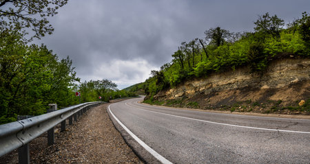 Empty long mountain road to the horizon on a sunny summer day with dramatic cloudy sky. Highway turn panoramic view. Woods rural freeway. Traffic background.の写真素材