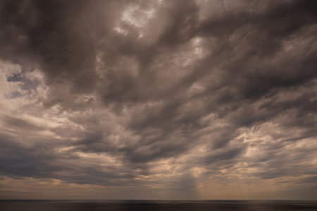 Sun between dark storm clouds over ocean. Dramatic seascape. Clouds and rain flurry over sea.の写真素材
