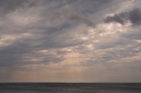 Sun between dark storm clouds over ocean. Dramatic seascape. Clouds and rain flurry over sea.の写真素材