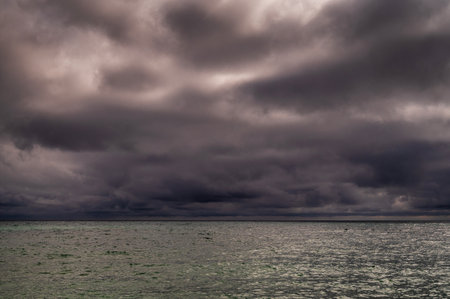 Sun between dark storm clouds over ocean. Dramatic seascape. Clouds and rain flurry over sea.の写真素材