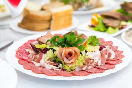 Plate of cold meats in the restaurant. Meat snacks. Smoked sausage and bacon, decorated with parsley...