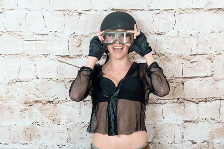 Fashion portrait of sexy stunning hipster woman, bright make up, vintage sunglasses, biker leather jacket, trendy jewelry and accessorizes. Urban wall background. Photoshoot relaxed bikerの写真素材