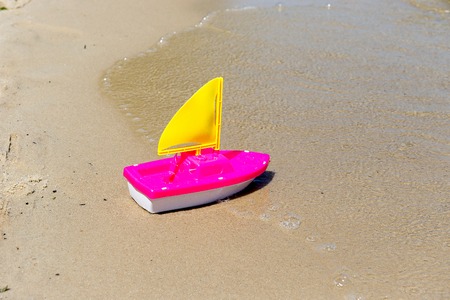 Toy boat in the wet sand of the sea. Summer holidays at sea. Boat trips.