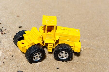 Toy tractor in the wet sand. Summer holidays at sea. Special miniature.