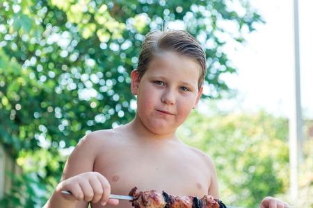 Tubby boy with pleasure eats a shish kebab. Camping. Healthy nutrition and diet.の写真素材