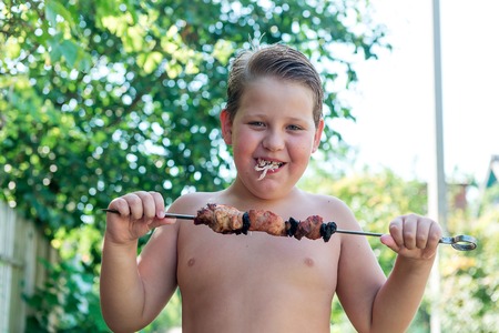 Tubby boy with pleasure eats a shish kebab. Camping. Healthy nutrition and diet.の写真素材