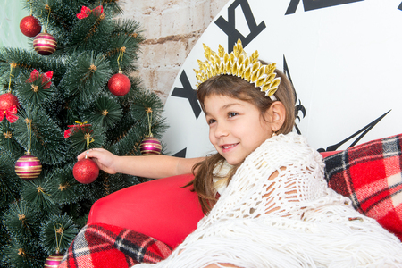 The child, a little girl sitting near a well-dressed Christmas tree and unwraps a gift.の写真素材