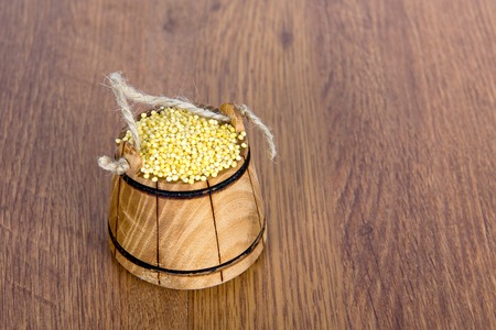Wooden bucket with millet on a wooden table. The most useful and tasty cereal porridge out of it.の写真素材