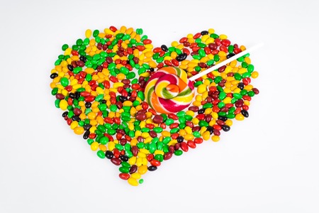 Coloured jelly beans are scattered in the shape of a heart and a lollipop in the form of an arrow on...