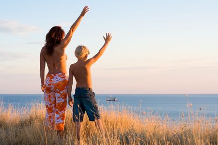Happy mother and son wave hands at sunsetの写真素材