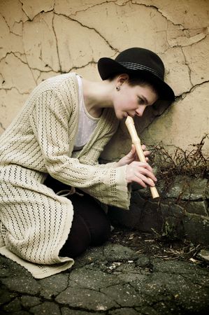 Young girl in a hat playing flute on the street