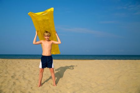Young boy with air mattress on summer beachの写真素材
