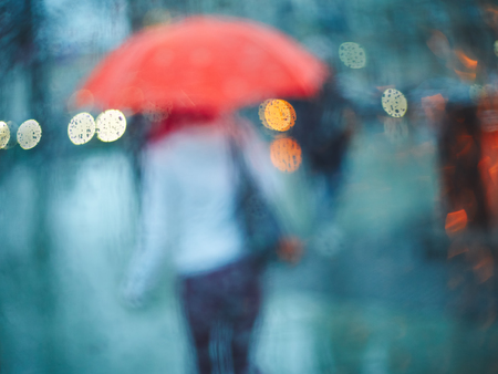 Young girl with an umbrella through a glass with rain drops. Blur bokeh, defocused backgroundの写真素材