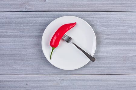 Top view of white dish with chili pepper on background of wooden tableの写真素材