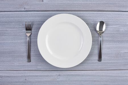 Top view of white dish with fork and spoon on background of wooden table