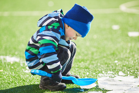 Little boy on a frozen playground breaks ice shovelの写真素材