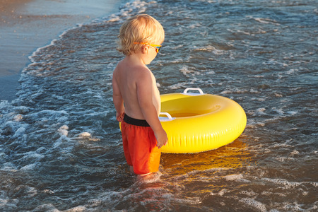 Blond boy in sunglasses with inflatable ring on the sea beachの写真素材