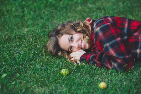Beautiful young woman in a male flannel shirt lying on green grass. Outdoor portrait in city parkの写真素材