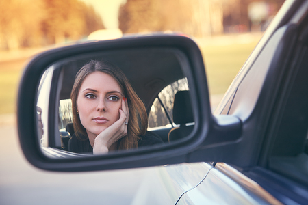 Rear view of attractive young woman in casual wear looking in rear-view mirror in her carの写真素材