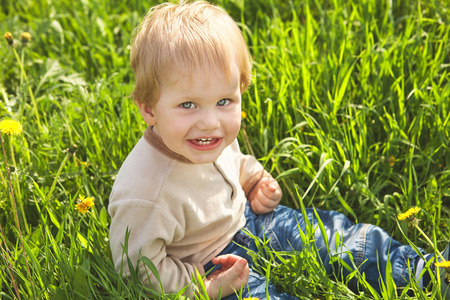 Happy childhood outdoor, little blond boy in green grassの写真素材