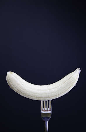 Banana at the fork, fresh tropical fruit detail in fork on black background, sweet fruit, dietの写真素材