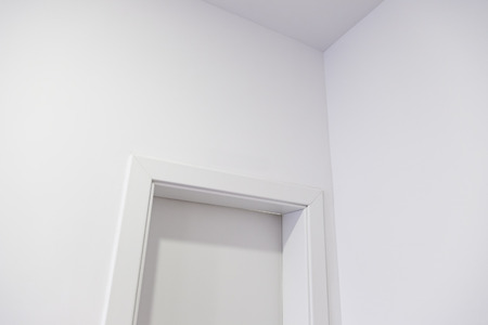 White door in a white wall, detail of a white painted wall with a locked doorの写真素材