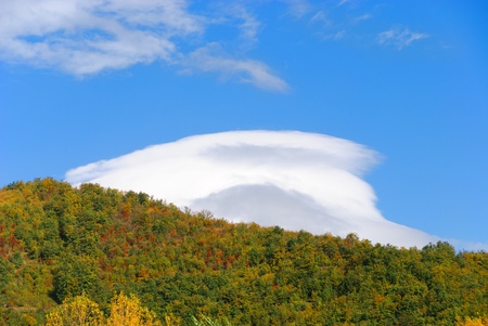 autumn trees and mountains with white clouds aboveの写真素材