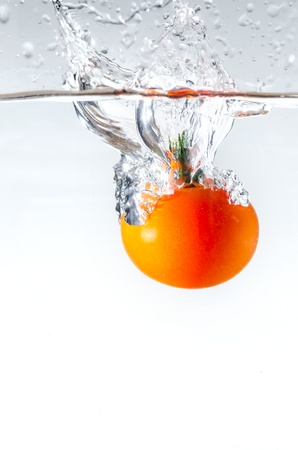 red tomato dropped into water with white backgroundの写真素材