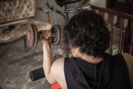A guy exercising at home with dumbbells, stretching, shoulder exercises and boxing warm-up